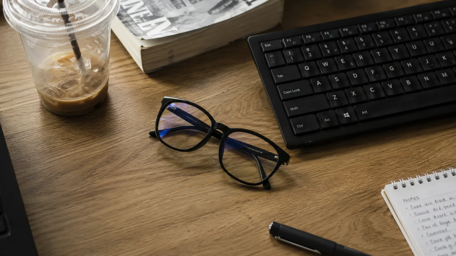 Pair of blue light glasses folded neatly on a desk next to a keyboard at the end of a workday