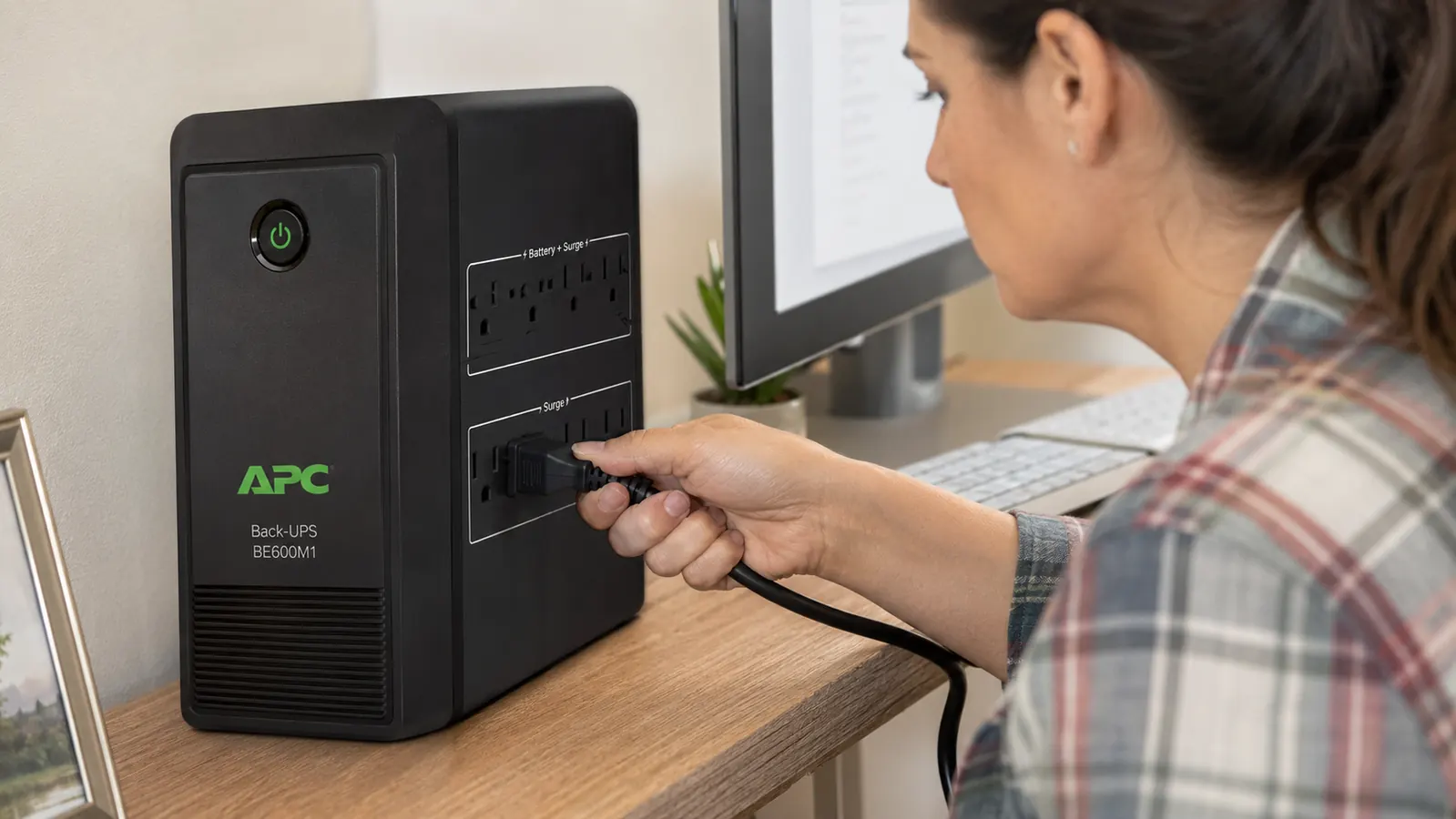 Close-up of a hand plugging a router power cord into the battery-backed outlets on the APC UPS