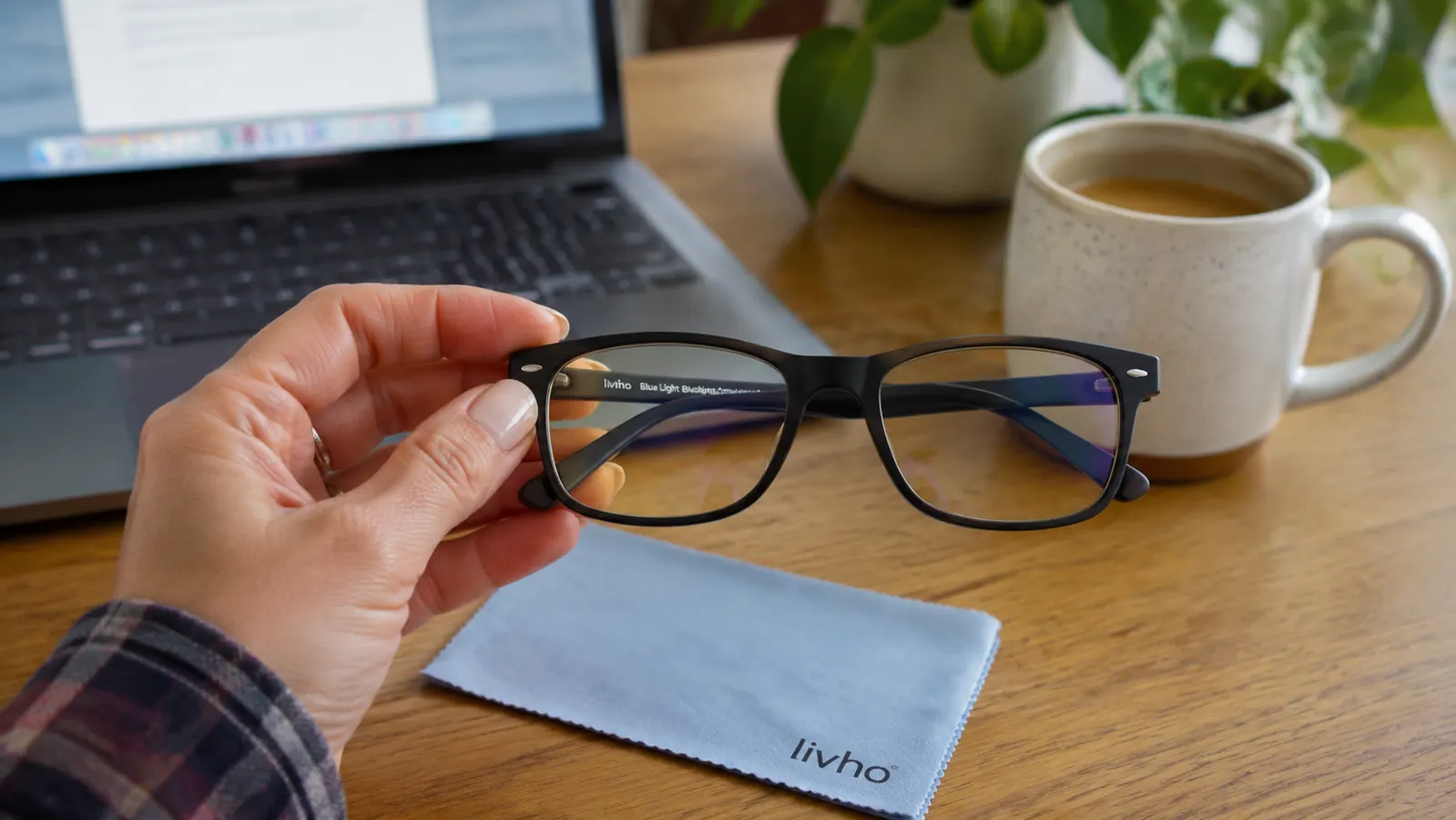 Hand holding the livho blue light glasses up next to a laptop keyboard