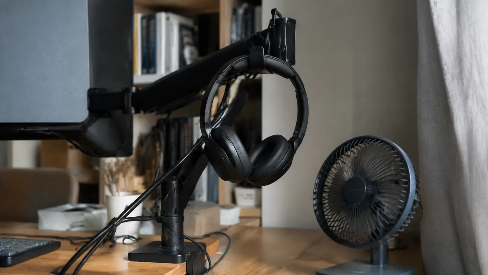 Logitech H390 headset hanging on a monitor arm hook next to a small desk fan