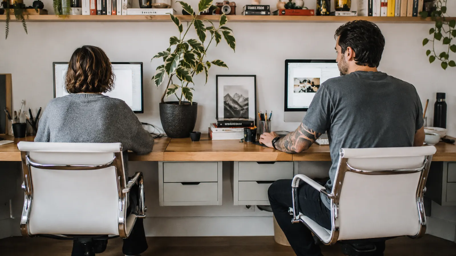 Two people at a shared home office desk each reaching for their own under desk drawer